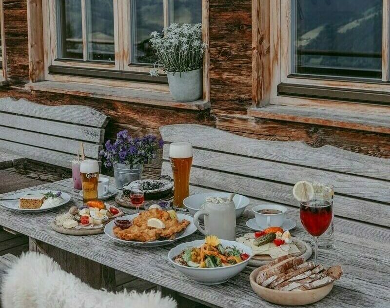 Ein gedeckter Holztisch auf der Seidlalm Terasse im Sommer, mit Speisen und Getränken.