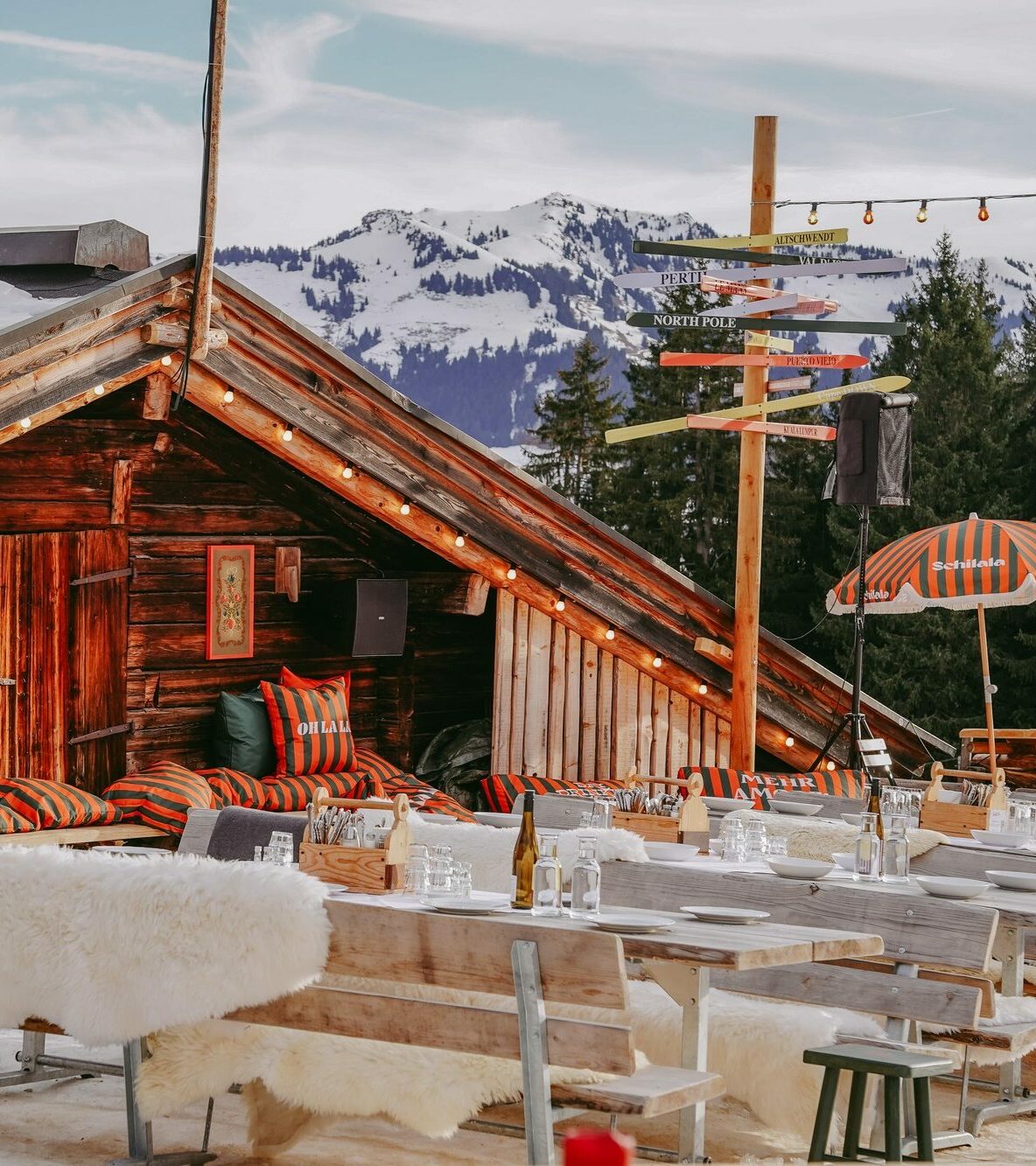 Seidlalm Events auf der Schilala Aprés Ski Hütte - Terasse mit Bänken und Tischen und Orange/ Grün gestreiften Schilala Kissen.