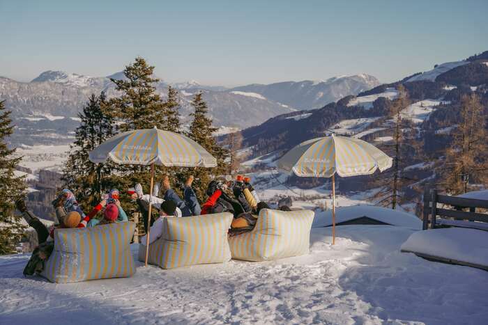 Mehrere Personen die Richtung Berge blickend auf gestreiften Schilala Säcken sitzen und Spaß haben.