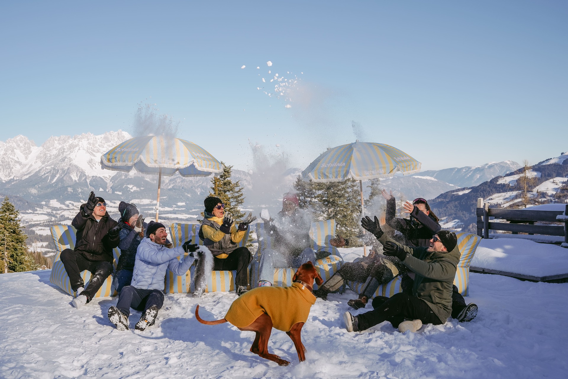 Mehrere Personen die auf der Schilala Aprés Ski Hütte in Kitzbühel auf blau gelben Sitzsäcken sitzen, im Schnell spielen mit Blick auf die Tiroler Berge.